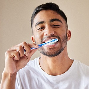 Man in white shirt smiling while brushing teeth