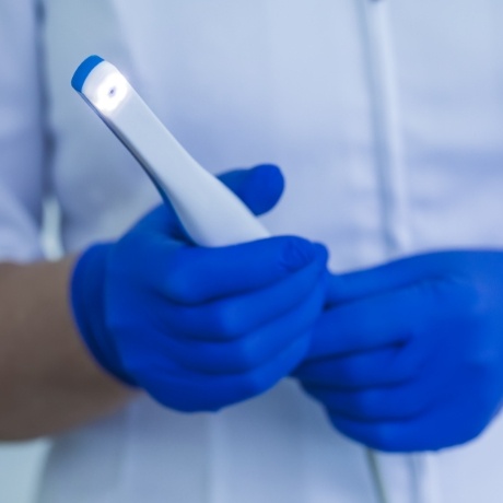 Gloved hands holding thin white intraoral camera