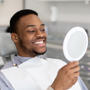 Man smiling at reflection in handheld mirror