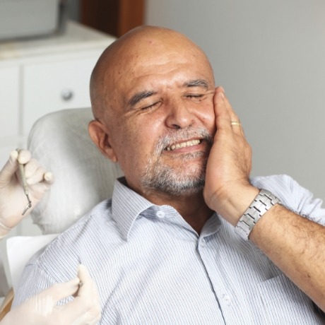 Man holding his cheek in pain while visiting emergency dentist in Corinth