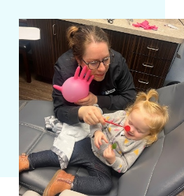 Dental team member showing dental mirrors to young child in dental chair