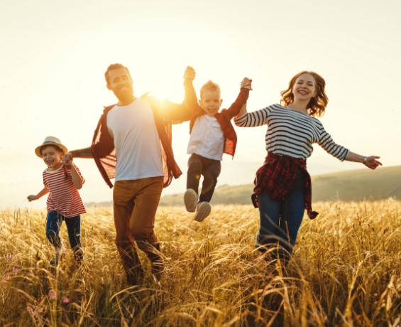 Family of four holding hands and walking through grass