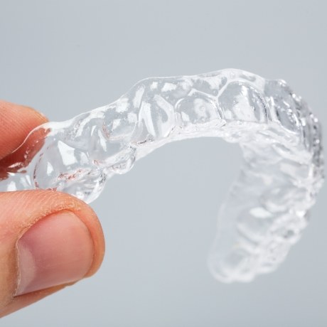 Close up of a hand holding a clear aligner