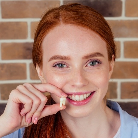 Smiling woman holding an extracted tooth